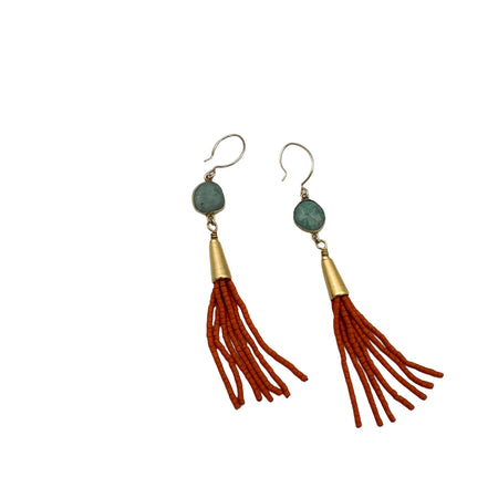 Pair of earrings with green beads and red tassels on a light gray background