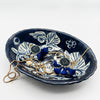 Navy blue ceramic jewelry dish with decorative patterns holding jewelry on a white background
