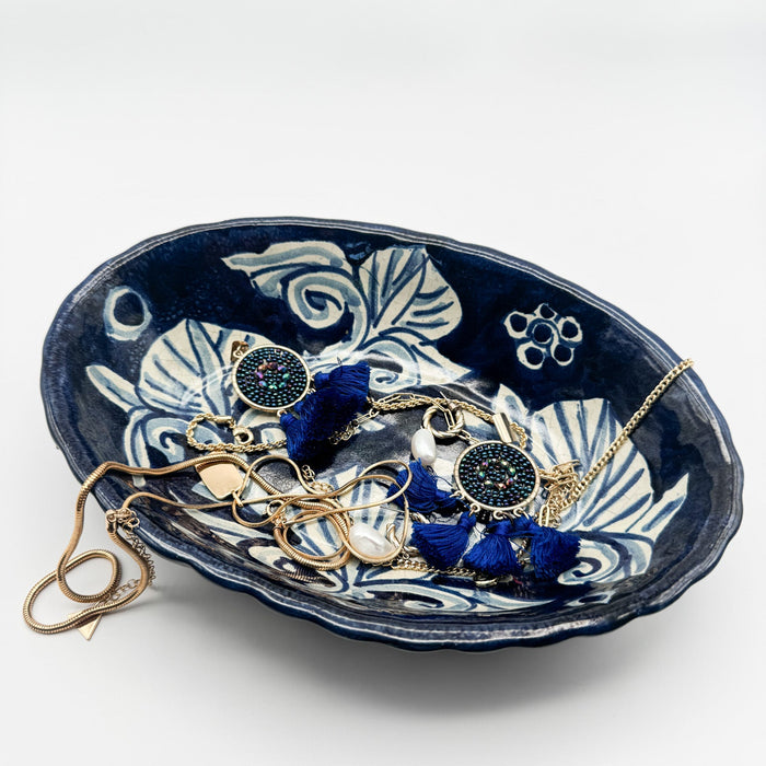 Navy blue ceramic jewelry dish with decorative patterns holding jewelry on a white background